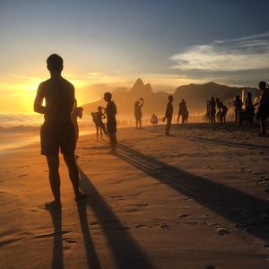 Silhouette people at beach against sky during sunset