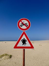 Close-up of information sign at sandy beach against clear blue sky