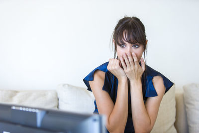 Shocked woman watching television while sitting on sofa at home