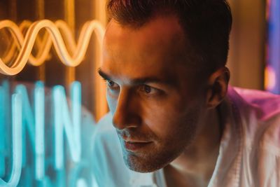 Close-up portrait of young man next to neon light