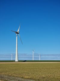 Wind turbines on field against clear blue sky