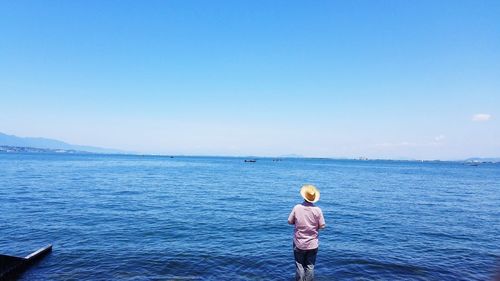 Rear view of man standing in sea against sky