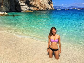 Portrait of young woman in bikini kneeling on shore at beach