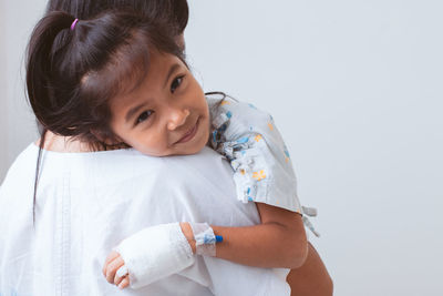 Mother carrying sick daughter against wall in hospital