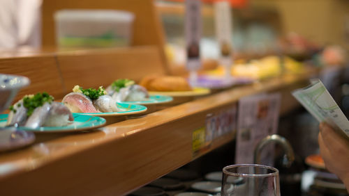 Cropped image of person holding menu by dishes served on counter in restaurant