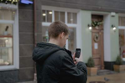 A guy in a jacket photographs a city street on a mobile phone, holds a smartphone in his hands