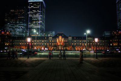 People on footpath against illuminated buildings at night