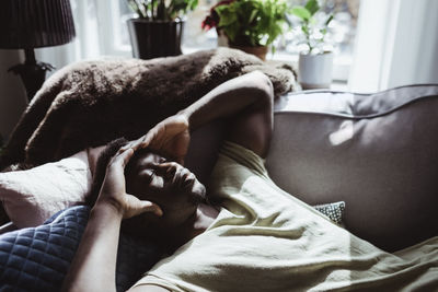 High angle view of man with headache lying on sofa at home