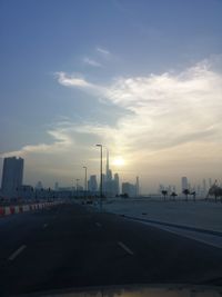 City street by buildings against sky during sunset