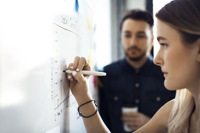 Businesswoman writing on whiteboard while male colleague standing in background