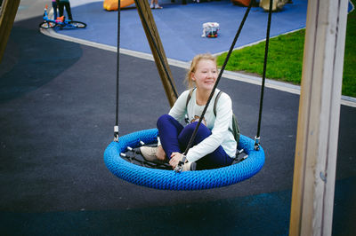 Smiling teenage girl sitting on swing at playground