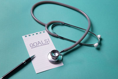 High angle view of stethoscope with paper and pen over blue background