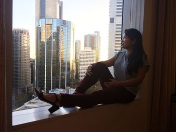 Smiling young woman looking through window while sitting at home