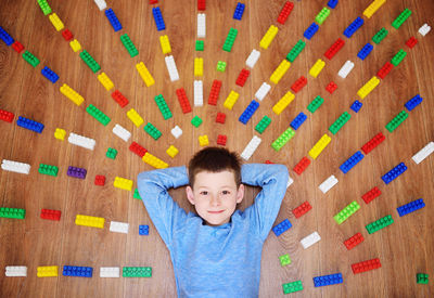 Portrait of smiling boy lying on floor with toy blocks