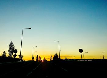 Road by silhouette trees against clear sky during sunset