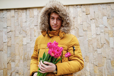 Blond man in a yellow winter jacket with a bouquet of tulips in hands