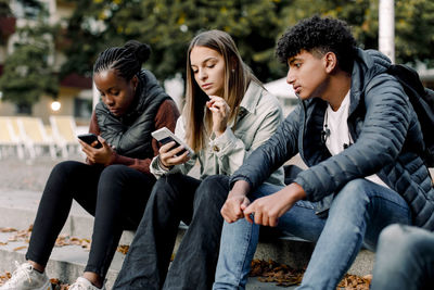 Teenage girls using smart phone while sitting with friend on steps in city