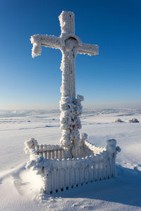 Cross on snow covered land against sky