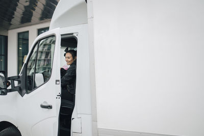 Smiling female worker closing door of white delivery van