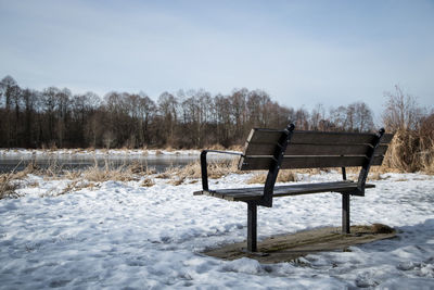 Empty bench on snow covered field against sky