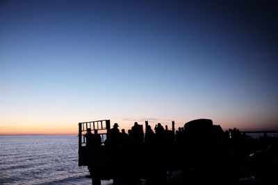 Silhouette people by sea against clear sky during sunset