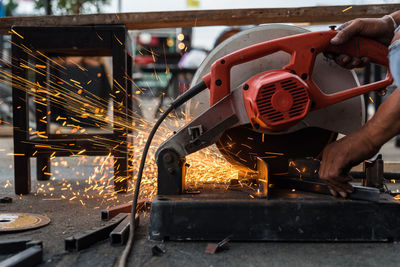 Cropped hands of man cutting metal with electric saw