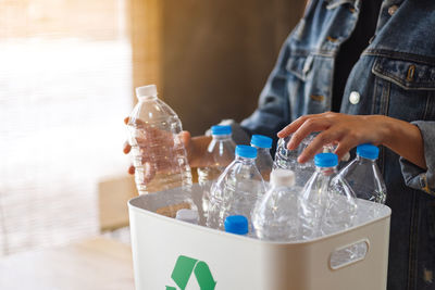 A woman collecting and separating recyclable garbage plastic bottles into a trash bin at home