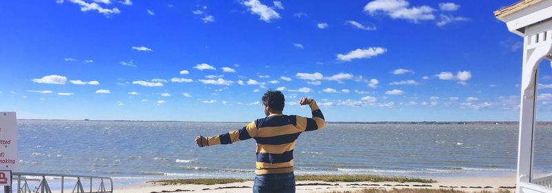 Rear view of man standing on beach against sky