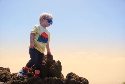 Full length of boy standing on rock against sky