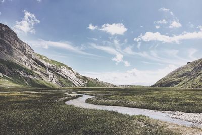 Stream on field amidst mountains against sky