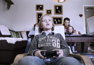 Little boy playing video game at home with family in background