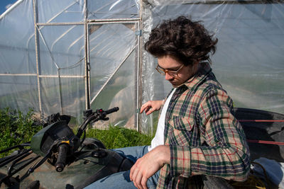 Young farmer in flannel shirt contemplates on stopped atv outside vegetable greenhouse