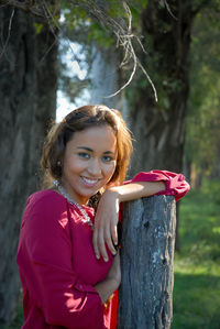 Portrait of a smiling young woman standing against trees