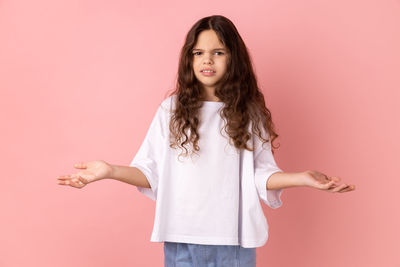 Portrait of young woman standing against pink background