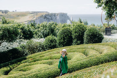 Portrait of a girl in a straw hat in a botanical garden with geometric bushes.