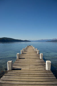 Pier over sea against clear blue sky