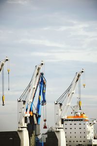 Cranes at harbor against sky