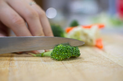 Cropped hand on woman cutting broccolini in kitchen