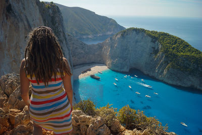 Rear view of mid adult woman with dreadlocks looking at sea while standing on mountain during sunny day