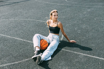 A basketball player is sitting on a sports field with a basketball and looks away. sport