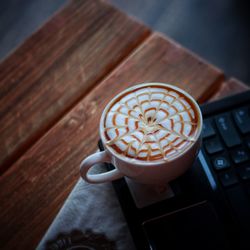 High angle view of coffee cup with froth art on computer keyboard at table