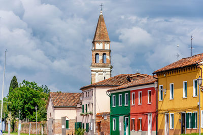 Clock tower by buildings in city against cloudy sky