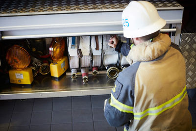 Rear view of firefighter arranging fire hose in engine at fire station