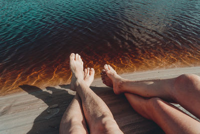 Legs of a man and a woman by the river against reddish water in the background. 