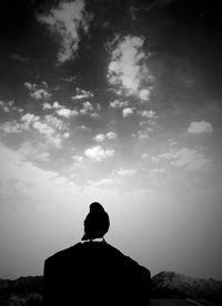 Rear view of silhouette man looking at rock against sky