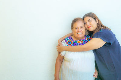 Portrait of granddaughter hugging her grandmother with love, standing against white background