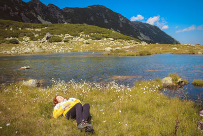 Full length of woman lying on grassy field by river against mountains