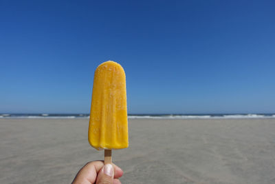 Close-up of hand holding ice cream on beach against clear blue sky