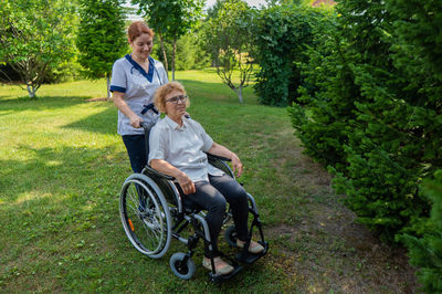 Caucasian female doctor walks with an elderly patient in a wheelchair in the park. nurse accompanies