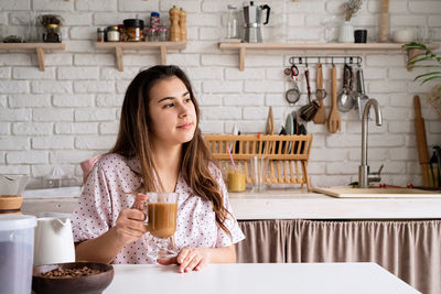 Portrait of smiling young woman making coffee in a kitchen 